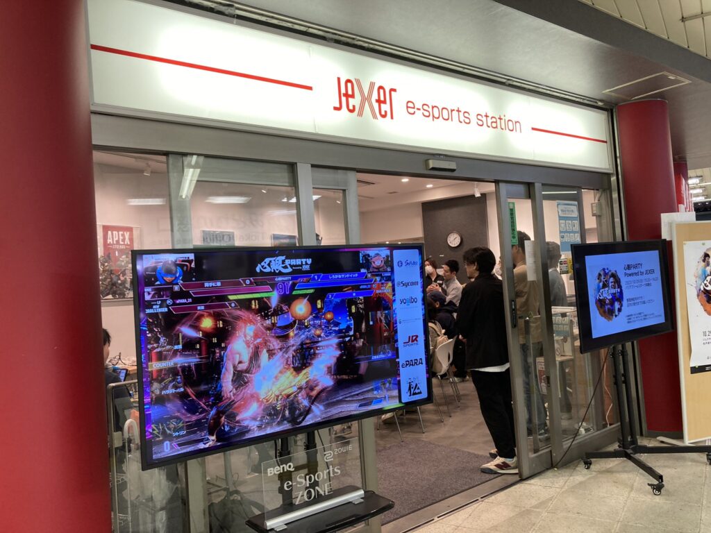 ジェクサー・eスポーツ ステーションの店舗前。大きいディスプレイにゲームプレイの様子が、小さいディスプレイに心眼パーティーの概要が表示されている。