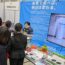 ブースに立って話す直也。手前の机にゲームコントローラーなどが置かれている