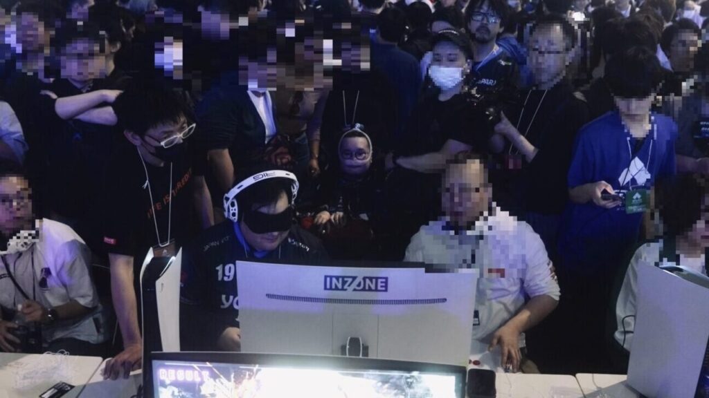 人で埋め尽くされた広い会場で、対戦台でゲームをプレイする直也