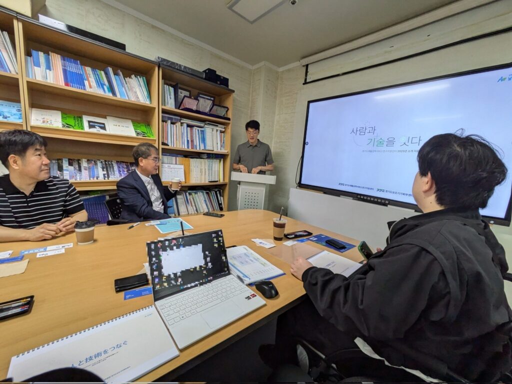机を取り囲んで座り、壁のスクリーンにスライドを映しながら意見交換する様子