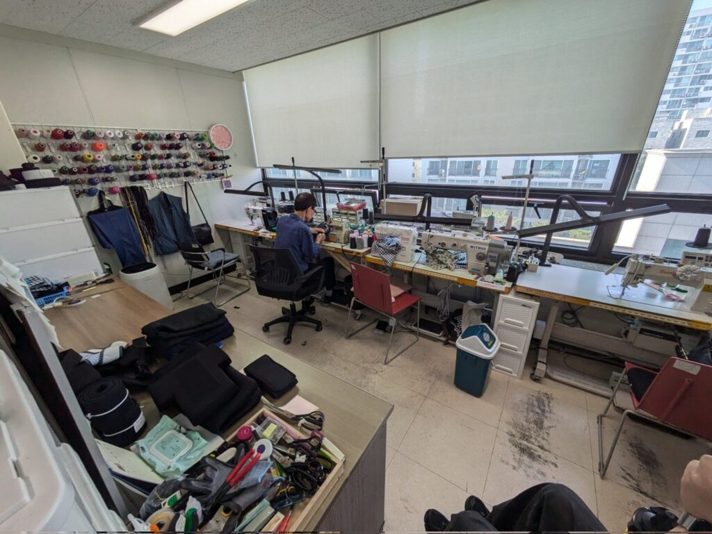 ミシンが並んだ作業台で一人の人が作業をしている様子。室内にはさまざまな裁縫道具や糸などがある