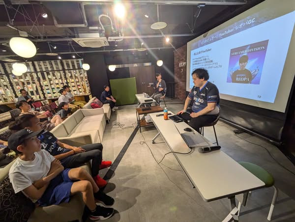 イーパラのユニフォームを着て会場正面に座るなおや、マイクを持って話すインタビュアー、話を聞く人々