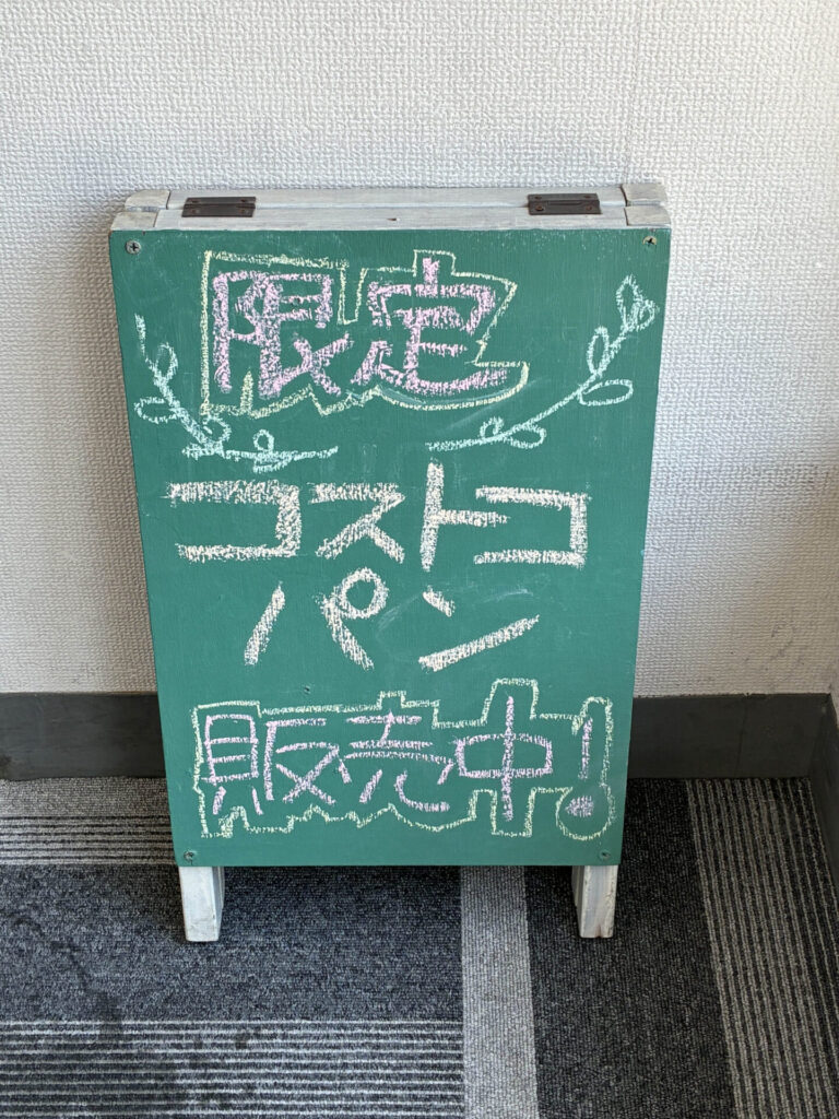 利用者さんが手書きで作成した「限定コストコパン販売中！」の黒板。イベント当日の会場入口でお客様をお迎えしました。