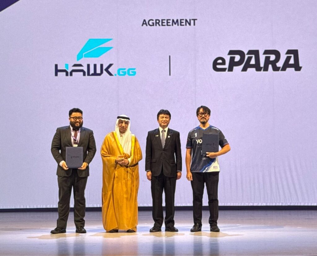 Hawk Gaming Groupとイーパラのロゴが映し出されたステージで覚書を手に持ち記念写真に写るePARA加藤ら4人