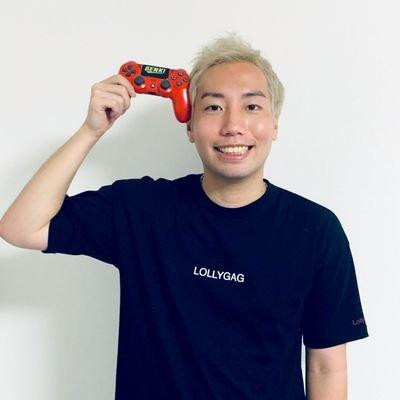 赤いゲームコントローラーを持ちポーズをとり、金髪のGENKIモリタがこちらを向いてにこやかな表情をしている写真