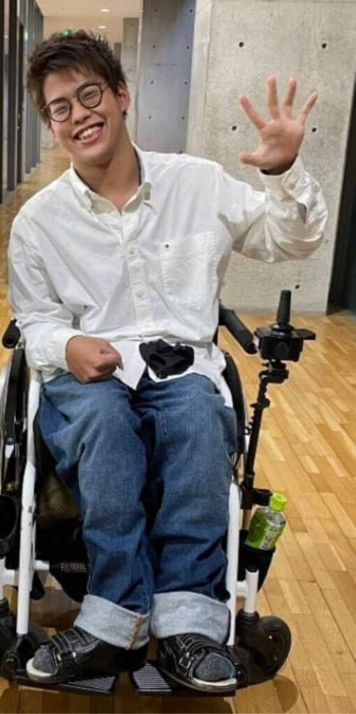 明るい笑顔で手を振り車椅子に乗る鱒渕羽飛の写真