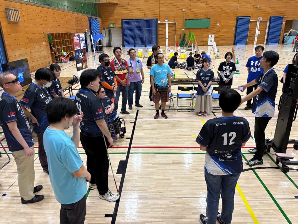 輪になって並んで打ち合わせを行う十数名のスタッフ