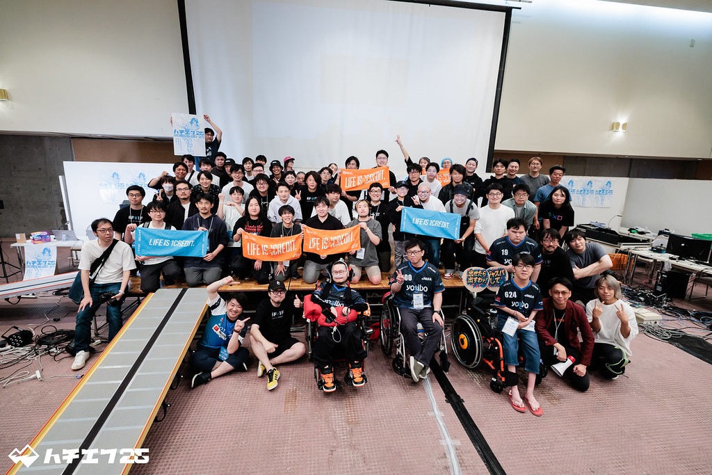 ハチエフ25の参加者集合写真。手前中央にプロデューサーのJeniがおり、まるぽす氏やだいじろう氏が並び、その後ろに参加者が集まっている。イベントタオルを広げている人も。