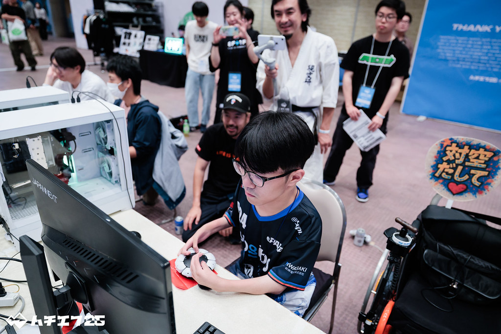 Access コントローラーでプレイするだいじろうさんをハンサム折笠さんや他の参加者が後ろから観戦する様子