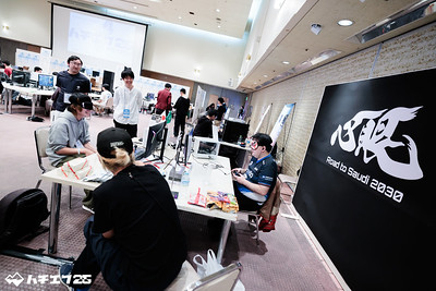 アイマスクをしたNAOYA選手と、同じくアイマスクをした参加者が対戦する様子。NAOYA選手の後ろに大きく「心眼　Road to Saudi　2030」と書かれたパネルが置かれている