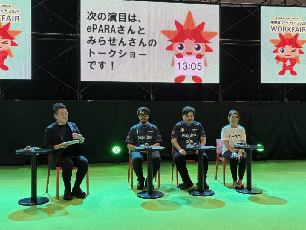 ステージ上で4人が並んで椅子2座っている様子。背後の大きい画面に「次の演目は、ePARAさんと みらせんさんの トークショーです」と表示されている