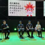 ステージ上で4人が並んで椅子2座っている様子。背後の大きい画面に「次の演目は、ePARAさんと みらせんさんの トークショーです」と表示されている