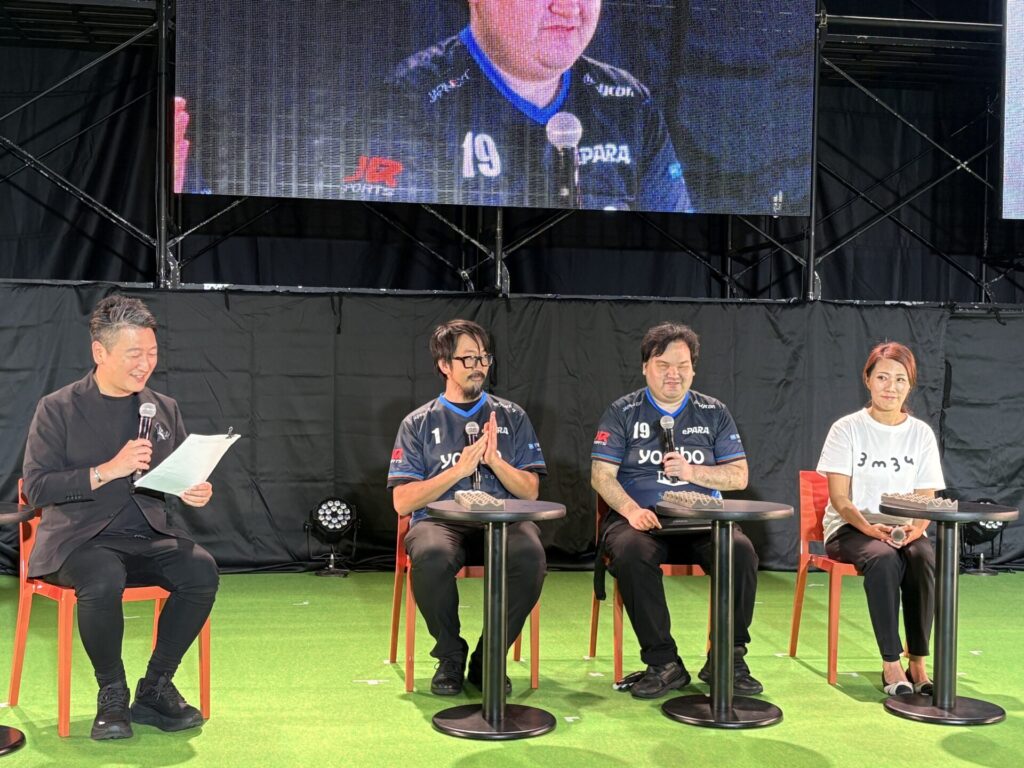 マイクを持って話す直也と隣で拍手する加藤