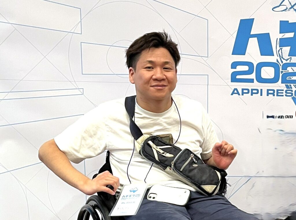 ハチエフ25のキービジュアルパネルの前で笑顔を見せるゆうたろうさん