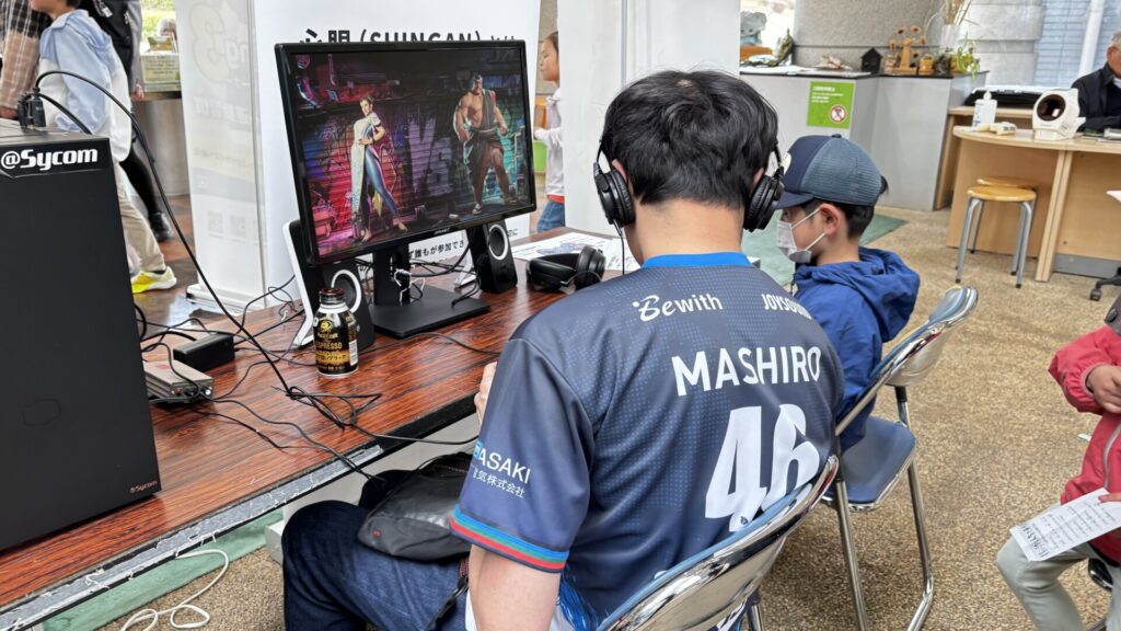 ヘッドホンを着けてストリートファイター6で子どもと対戦するましろ