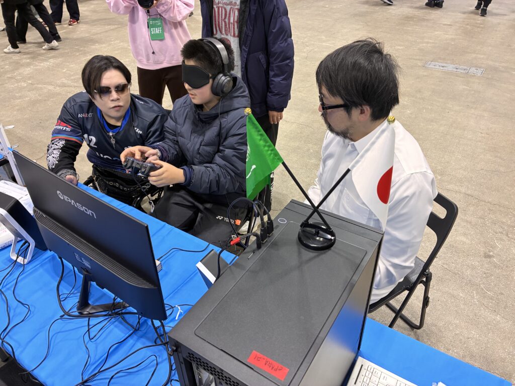 参加者が「心眼」体験を行う様子。(前景)
心眼「Road to Saudi 2030」を軸としたサウジアラビア連携・バリアフリーeスポーツ体験ブースでは、「ePARA × Saudi Vision 2030」の取り組み紹介および、心眼体験(ストリートファイター6体験)が行われた。