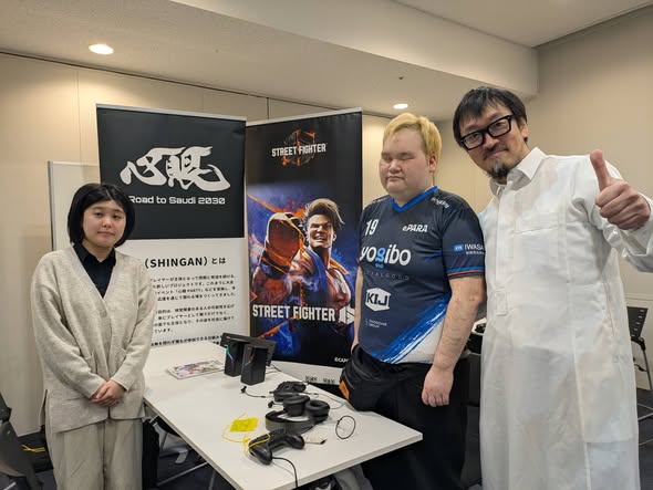 ゲームコントローラーやヘッドホンなどを置いたブースに笑顔で立つ加藤と北村。背後にはePARAのプロジェクト「心眼」（心の目）のパネルとストリートファイター6のパネルが置かれている。