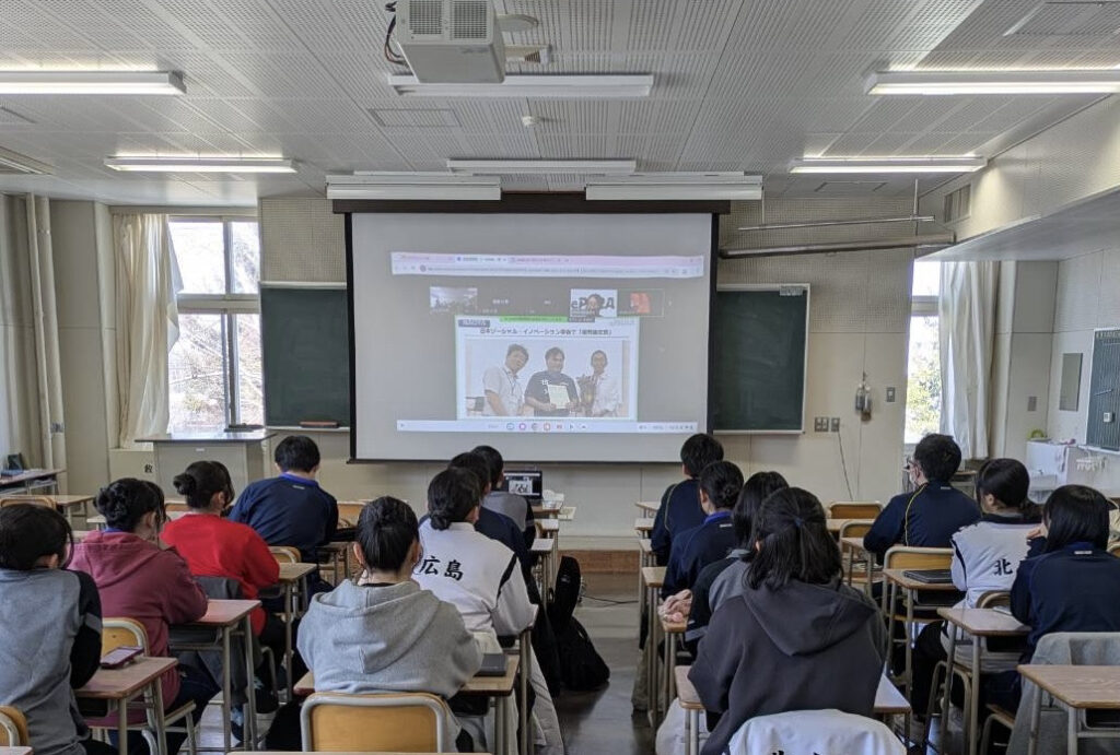 教室のスクリーンに投影された画像を見ながら話を聞く高校生たち