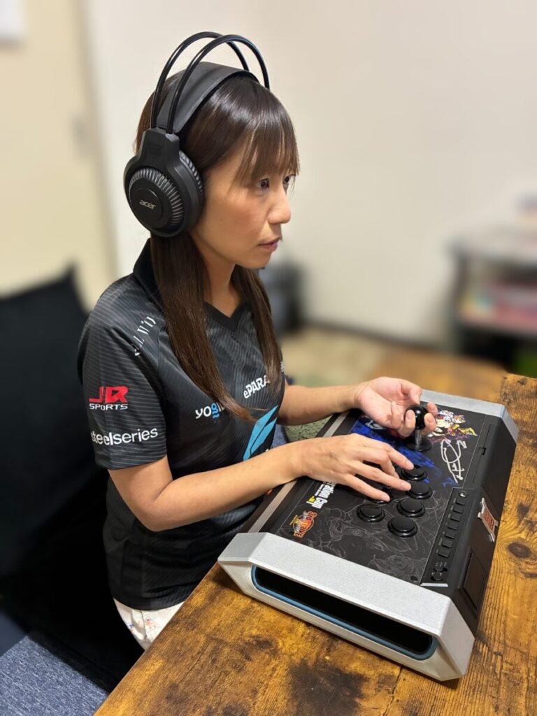 ヘッドホンを装着し、アーケードコントローラーを操作して格闘ゲームをプレイするタンパタメ子さん